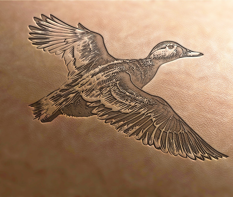 May include: A detailed, embossed image of a duck in flight, carved into a piece of leather. The duck is brown and white with a long, pointed beak.