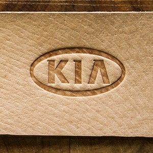 May include: A close-up of a brown leather patch with the word "KIA" embossed in an oval shape.