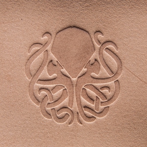 May include: Close-up of a tan leather surface with an embossed design. The design features a central geometric shape with stylized tentacles or tendrils radiating outwards. The texture of the leather is visible, adding depth to the image.