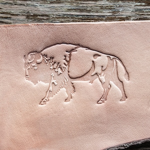 May include: A close-up of a light brown leather patch with a detailed embossed image of a bison.