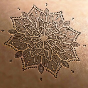 May include: A detailed mandala design is embossed into a piece of brown leather. The mandala features intricate floral patterns and geometric shapes.