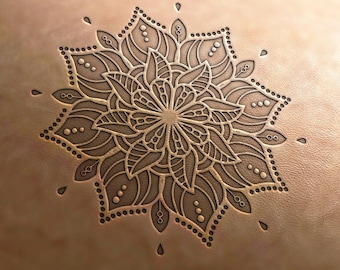 May include: A detailed mandala design is embossed into a piece of brown leather. The mandala features intricate floral patterns and geometric shapes.