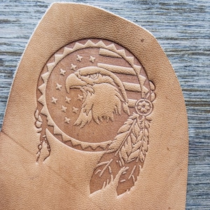 May include: A brown leather patch with an embossed design of an eagle's head with an American flag behind it and a feather dreamcatcher below.
