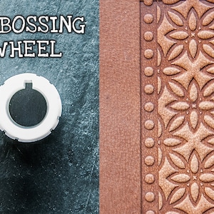 May include: White embossing wheel with a circular design. The wheel is on a dark grey surface. The design is embossed on a brown leather surface.