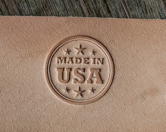 Könnte beinhalten: Nahaufnahme eines braunen Lederflecks mit einem runden geprägten Stempel, auf dem "MADE IN USA" mit fünf Sternen um den Umfang steht.