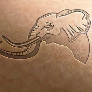 Puede incluir: Imagen en relieve de la cabeza y la trompa de un elefante sobre una superficie de cuero marrón claro. Los rasgos del elefante están intrincadamente tallados, mostrando la textura y la profundidad del diseño. La obra de arte está centrada, con el elefante mirando hacia la izquierda.