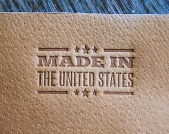 Könnte beinhalten: Nahaufnahme eines braunen Leder-Etiketts mit dem Text "MADE IN THE UNITED STATES", der in einem rechteckigen Rahmen geprägt ist.