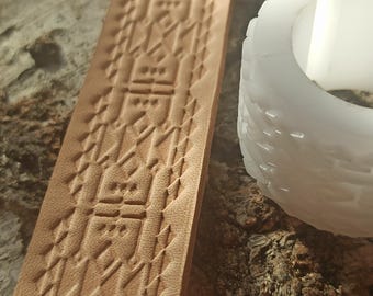 May include: A close-up of a light brown leather strip with a geometric pattern embossed into the surface. A white plastic stamp with a similar pattern is visible in the background.