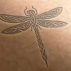 Op de afbeelding: Een gedetailleerd, ingewikkeld ontwerp van een libel in Keltische knoopwerk, gegraveerd in een lichtbruin lederen oppervlak.