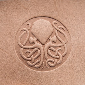 May include: A brown leather patch with a circular embossed design of a stylized octopus with a diamond shape in the center.