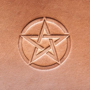 Puede incluir: Una superficie de cuero marrón con una estrella de cinco puntas en relieve en el centro. La estrella está rodeada por un círculo.