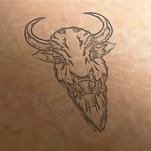 May include: A black and white line drawing of a bull's head on a light brown leather background.