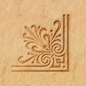 May include: A close-up of a brown leather surface with a decorative, embossed design in the corner. The design features a stylised floral motif with intricate swirls and lines.