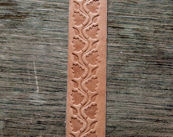 May include: A close-up of a brown leather strip with a repeating pattern of leaves embossed into the surface.