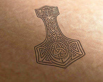 May include: A detailed, dark brown image of Thor's hammer, Mjolnir, carved into a light brown leather surface. The hammer features intricate knotwork and geometric designs, with a prominent circular emblem at the base.