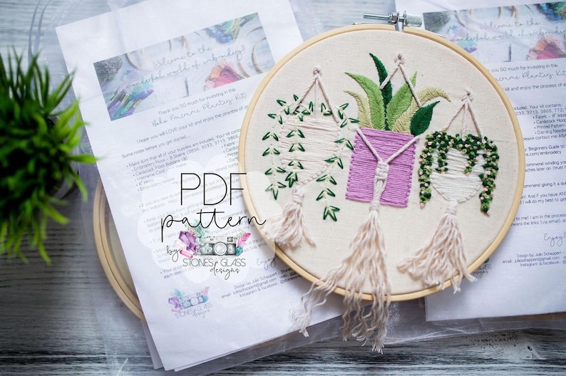 a hand-embroidered piece of art with a plant design, displayed alongside a printed pattern and instructions for creating the embroidery.