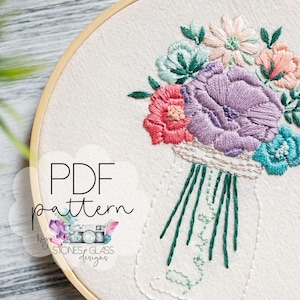Pode incluir: Buquê floral bordado em um aro de madeira. O buquê apresenta flores rosa, roxas e turquesas com folhas verdes. O texto "PDF pattern" é visível.