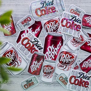 May include: A collection of stickers featuring Diet Coke and Dr. Pepper soda cans. The stickers are in various sizes and orientations, with the words "Diet Coke" and "Dr. Pepper" prominently displayed. The phrase "Maybe Diet Coke is addicted to me" is also visible.