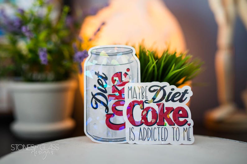May include: A Diet Coke sticker in the shape of a soda can and a smaller sticker with the text "Maybe Diet Coke is addicted to me." The can sticker has the word "Diet" in blue script.