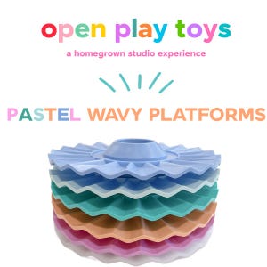 Puede incluir: Una pila de cinco plataformas circulares de bordes ondulados en colores pastel que incluyen azul claro, verde azulado, melocotón, rosa y blanco. El texto superior dice open play toys, a homegrown studio experience y PASTEL WAVY PLATFORMS.