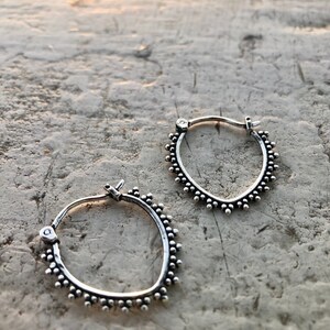 May include: A pair of silver hoop earrings with a beaded edge. The earrings are small and delicate.
