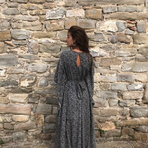 May include: A long black and white floral print maxi dress with a keyhole back and long sleeves. The dress is tied at the waist with a black ribbon.