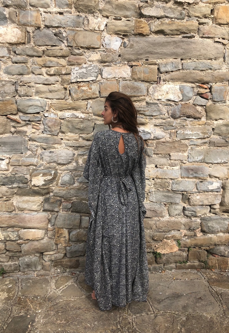 May include: A long black and white floral print maxi dress with a keyhole back and long sleeves. The dress is tied at the waist with a black ribbon.