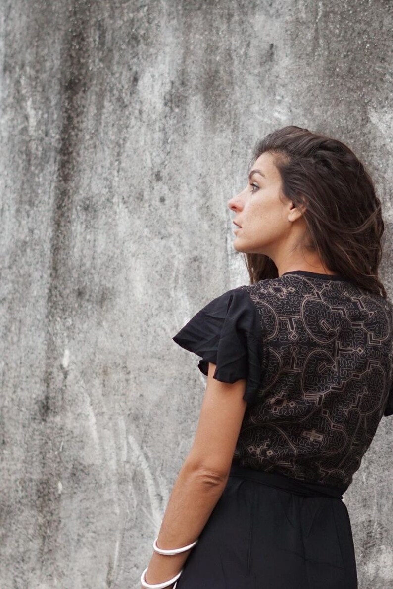 Peut inclure: Une femme portant une robe noire avec un motif g&eacute;om&eacute;trique brun. La robe a un col &agrave; volants et une taille cintr&eacute;e. Elle porte un bracelet argent&eacute; au poignet.