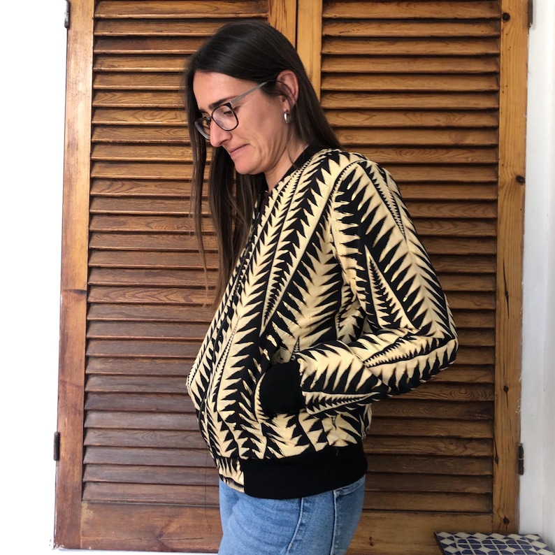 Puede incluir: Una chaqueta bomber negra y crema con un patr&oacute;n geom&eacute;trico. La chaqueta tiene una cremallera y pu&ntilde;os y cintura de canal&eacute;.
