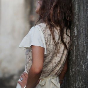 Peut inclure: Une femme portant une robe blanche avec un corsage &agrave; motifs marrons et blancs. La robe a un n&oelig;ud &agrave; la taille et la femme porte un bracelet en argent.