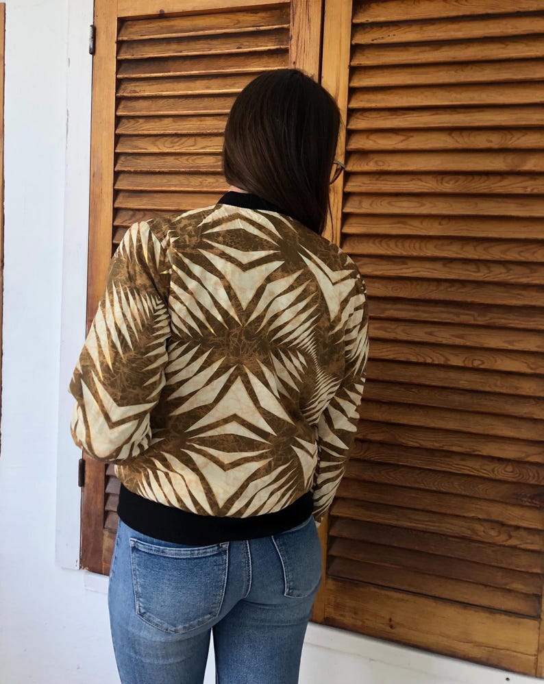 Puede incluir: Una chaqueta bomber con estampado marr&oacute;n y blanco con una banda negra. La chaqueta est&aacute; hecha de una tela suave y sedosa.