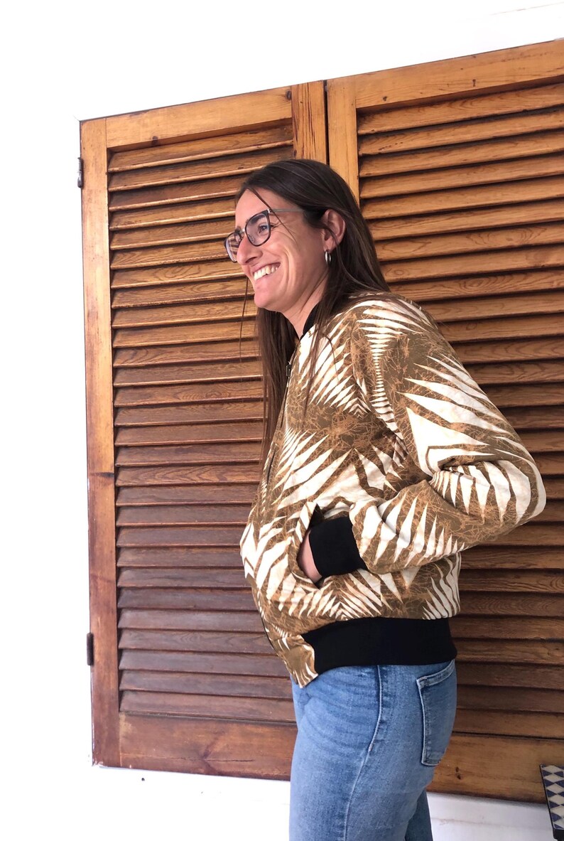 Puede incluir: Una mujer lleva una chaqueta bomber con estampado marr&oacute;n y blanco con ribetes negros. Est&aacute; sonriendo y mirando hacia un lado. La chaqueta tiene una cremallera y un cuello de pie.
