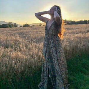 May include: A woman wearing a long, flowing, patterned maxi dress stands in a field of tall, golden wheat. The sun is setting behind her, creating a warm glow.