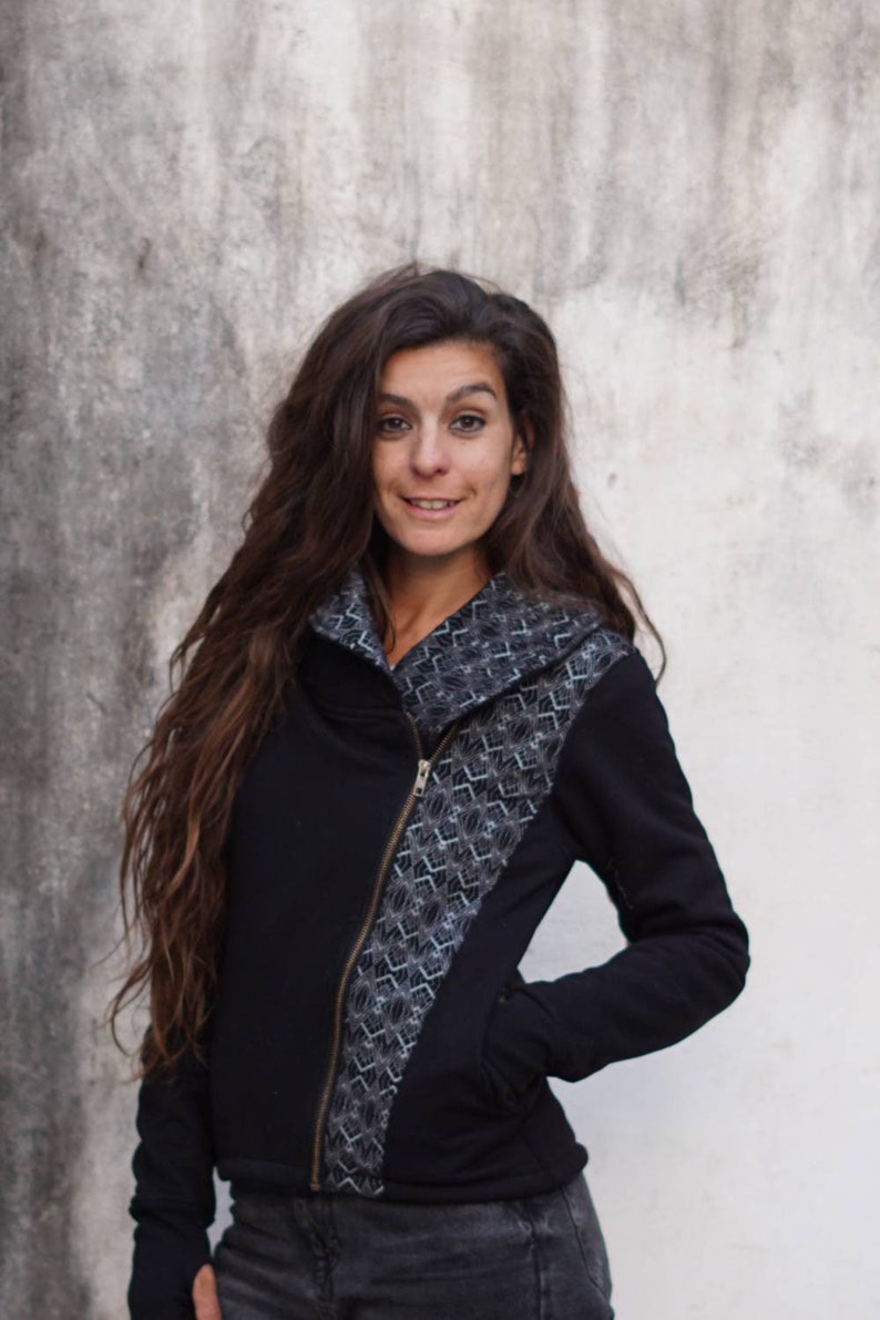 K&ouml;nnte beinhalten: Eine schwarze Rei&szlig;verschlussjacke mit einem geometrischen Muster auf der Vorderseite. Die Jacke hat einen hohen Kragen und lange &Auml;rmel.