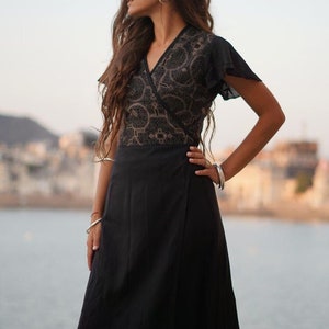 Peut inclure: Une robe noire portefeuille avec un corsage &agrave; motifs dor&eacute;s et noirs et des manches courtes. La robe est fluide et a une longue jupe.