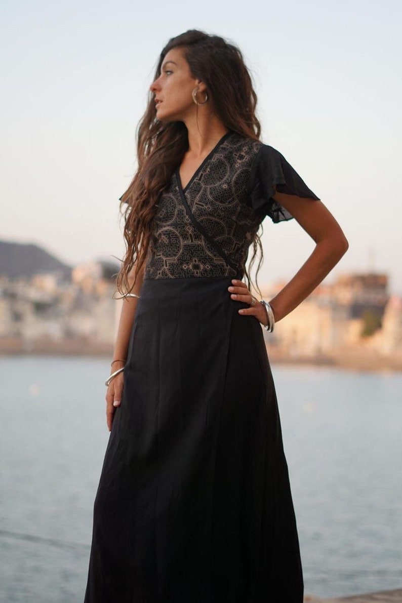Peut inclure: Une robe noire portefeuille avec un corsage &agrave; motifs dor&eacute;s et noirs et des manches courtes. La robe est fluide et a une longue jupe.