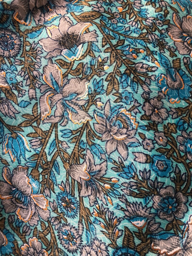 May include: A close-up of a teal fabric with a floral pattern. The flowers are in shades of blue, gray, and brown. The fabric has a subtle sheen.