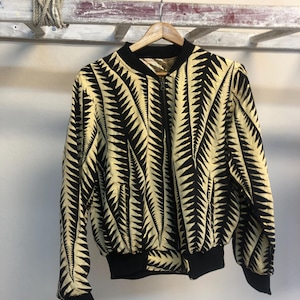 Puede incluir: Una chaqueta bomber negra y amarilla con un patr&oacute;n geom&eacute;trico. La chaqueta tiene una cremallera y pu&ntilde;os y cintura de canal&eacute;.