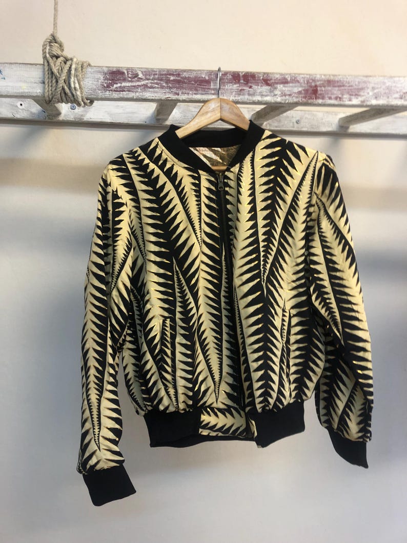 Puede incluir: Una chaqueta bomber negra y amarilla con un patr&oacute;n geom&eacute;trico. La chaqueta tiene una cremallera y pu&ntilde;os y cintura de canal&eacute;.