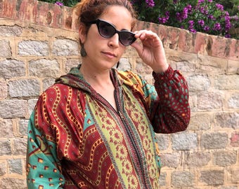 May include: A woman wearing a red, green, and gold patterned jacket with a zipper closure. The jacket has a hood and is made of a silky material.