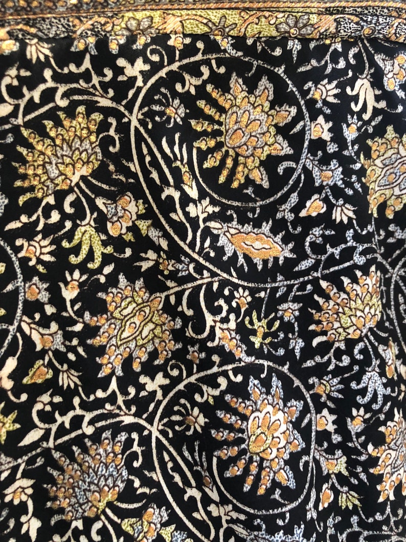 May include: Black fabric with a white and gold floral pattern. The pattern features intricate swirls and leaves.