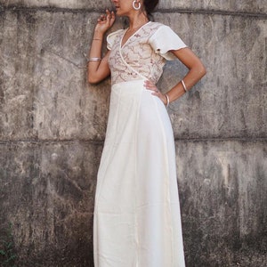 Peut inclure: Une robe blanche enroul&eacute;e avec un motif brod&eacute; brun. La robe a une manche courte et une jupe fluide. Le mannequin est debout devant un mur en b&eacute;ton.
