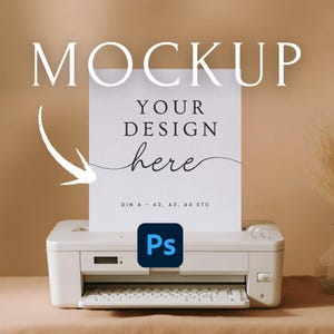 Puede incluir: Una impresora blanca con una hoja de papel que dice "MOCKUP" y "YOUR DESIGN here". Se está imprimiendo el papel. El logotipo de Adobe Photoshop está en la impresora.