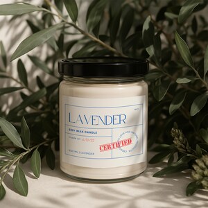 May include: A clear glass jar candle with a black lid. The label reads "LAVENDER SOY WAX CANDLE made on 6/10/22 350 ML | LAVENDER" with a red "CERTIFIED" stamp. The jar is surrounded by green foliage.