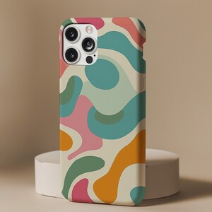 Pu&ograve; includere: Una custodia per telefono bianca con un design astratto colorato con forme rosa, blu, verdi e arancioni. La custodia ha un ritaglio per l'obiettivo della fotocamera.