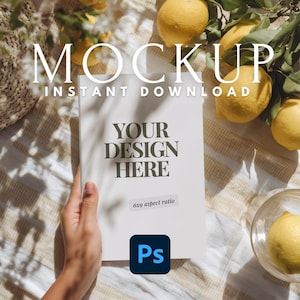 May include: A white book mockup with the text "MOCKUP INSTANT DOWNLOAD" at the top. The book has the text "YOUR DESIGN HERE" and a "6x9 aspect ratio" sticker. Lemons and foliage surround the book.
