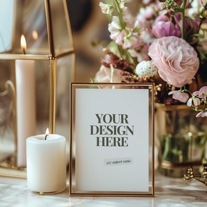 May include: A gold-framed picture frame with a white background and the text "YOUR DESIGN HERE 5x7 aspect ratio". The frame is sitting on a white surface with a lit candle and a gold lantern in the background.