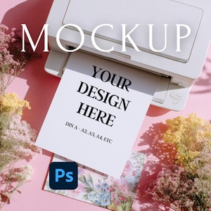 May include: A white printer printing a paper with the text "YOUR DESIGN HERE" in black. The word "MOCKUP" is at the top. The paper also includes "DIN A-A2, A3, A4, ETC". A Photoshop logo is in the corner. The background is pink with flowers.