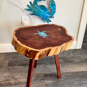 May include: A wooden end table with a live edge top and three legs. The top features a blue and green resin turtle inlay.