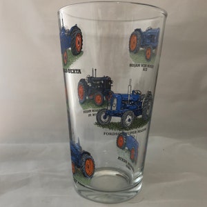 May include: A clear glass pint glass with a blue and orange design featuring different Fordson tractors. The glass has the text "Fordson Super Major" printed on it.